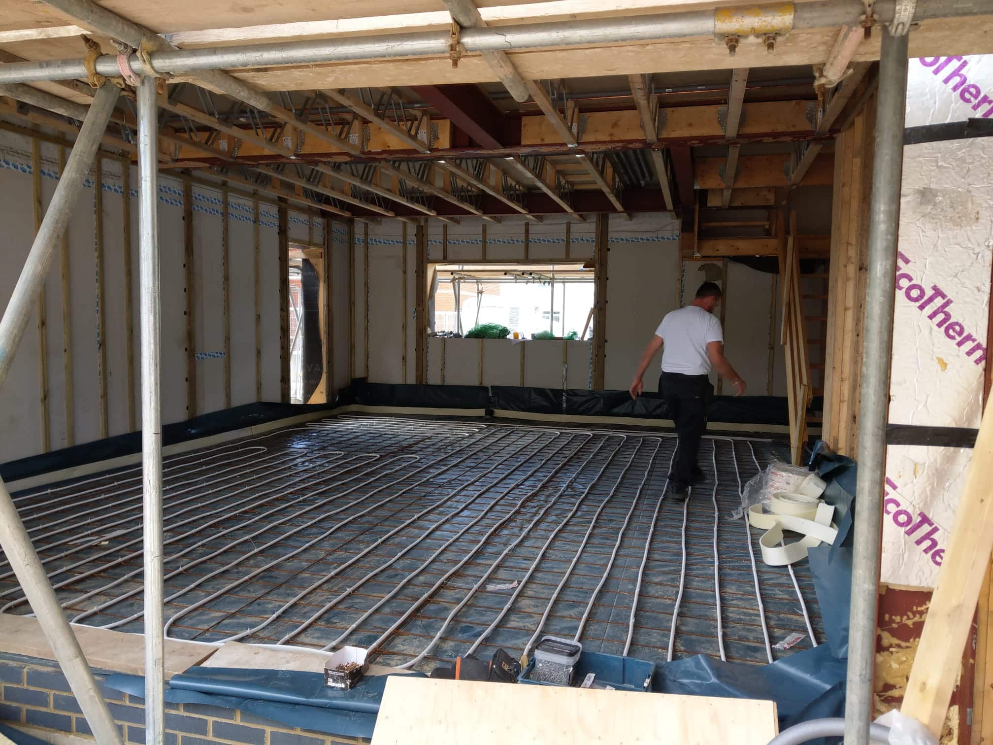 Person installing underfloor heating pipes in a house under construction.